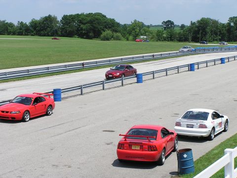 1993 Ford Taurus - A red Ford Mustang is parked on a race track with other vehicles in the background.