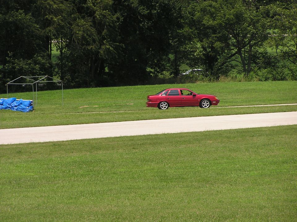 Red 1993 Ford Taurus sedan driving on a track, side view