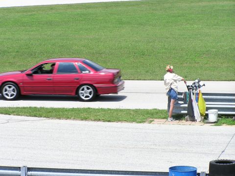 1993 Ford Taurus - A red 1993 Ford Taurus sedan drives past a flagger on the side of a racetrack.