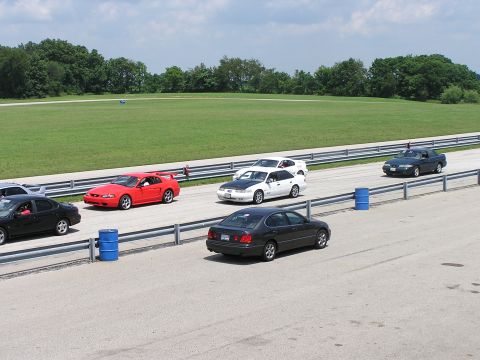 1993 Ford Taurus - Several cars are on a racetrack, with a dark sedan in the foreground and a red sports car further ahead.