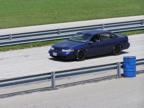 1993 Ford Taurus - A blue sedan is on a race track with a blue barrel nearby.