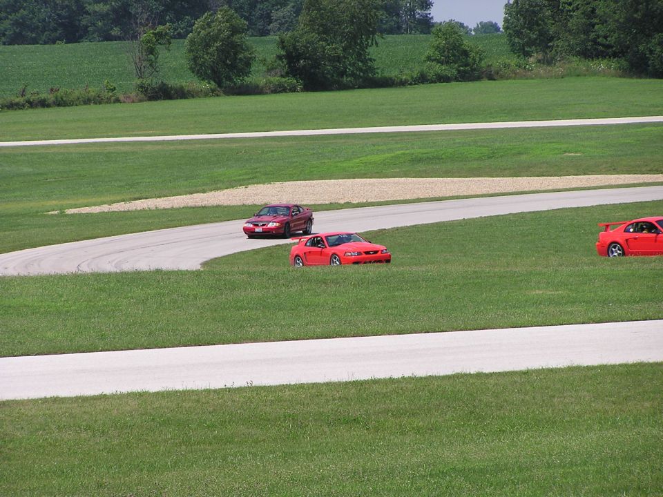 Three red sports cars on a race track, one in the foreground, two in the background