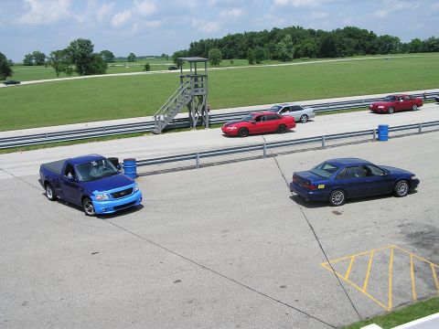 1993 Ford Taurus - Blue Ford F-150 Lightning pickup truck on a racetrack with other vehicles present.
