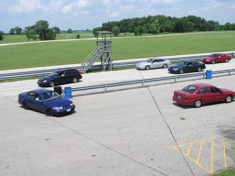 1993 Ford Taurus - Several cars are on a racetrack, including a blue 1993 Ford Taurus in the foreground.