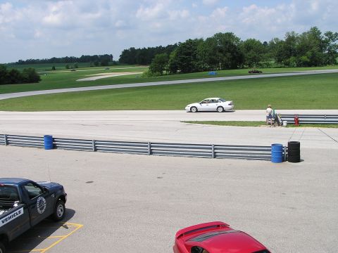 1993 Ford Taurus - A white 1993 Ford Taurus sedan is seen on the race track with other vehicles in the background.