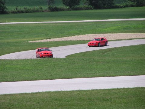 1993 Ford Taurus - Two red Ford Mustang Cobras navigate a turn on a race track during a sunny day.