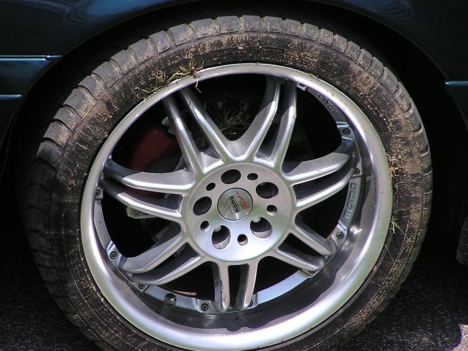 Close-up of a silver multi-spoke aftermarket wheel with a 'Momo' logo and a worn tire with grass and dirt