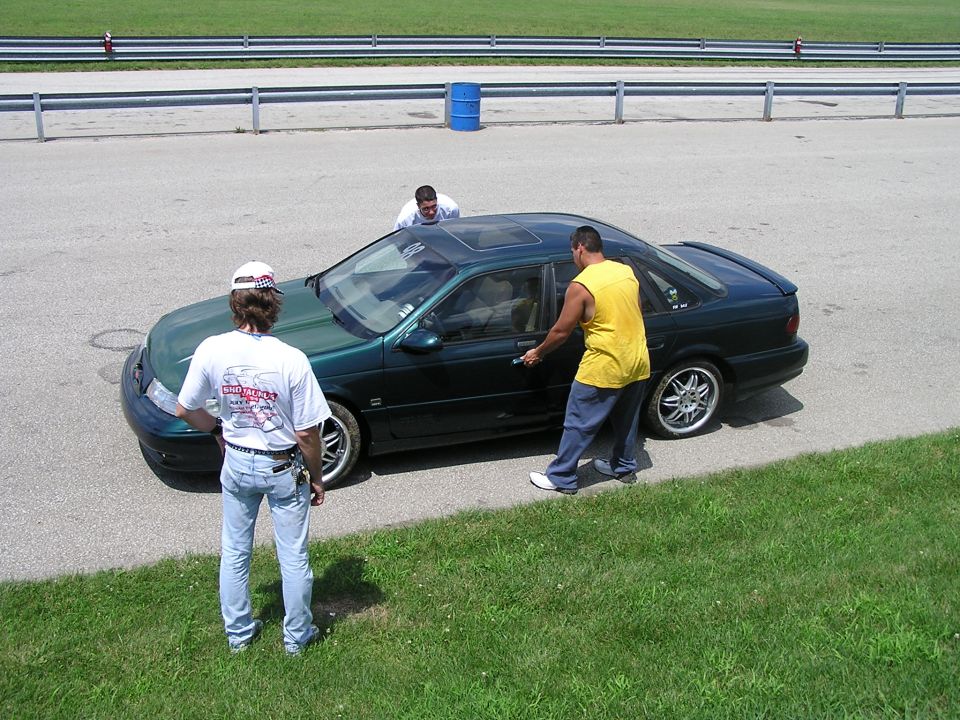 Dark green sedan with sunroof, people around it on a track