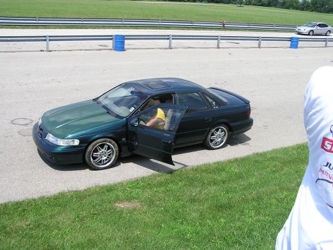 1993 Ford Taurus - A dark green sedan is parked on the side of a track with its driver's door ajar.