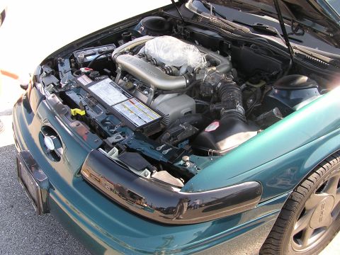 1993 Ford Taurus - The engine bay of a green 1993 Ford Taurus is visible with the hood open, revealing the V8 engine and battery.