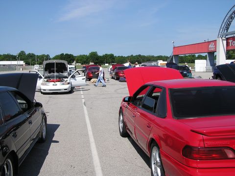 1993 Ford Taurus - Multiple cars are parked on a sunny day at an outdoor event, with some hoods open.