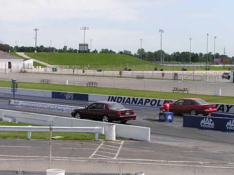1993 Ford Taurus - Two sedans are side-by-side on the drag strip at Indianapolis Raceway Park, with a person in red watching from the side.