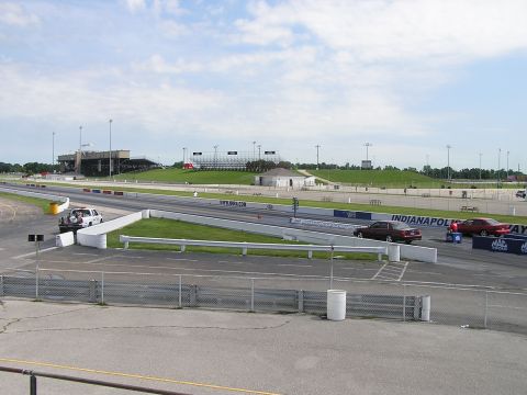 1993 Ford Taurus - View of a drag strip with spectator stands and several vehicles on the track under a cloudy sky.