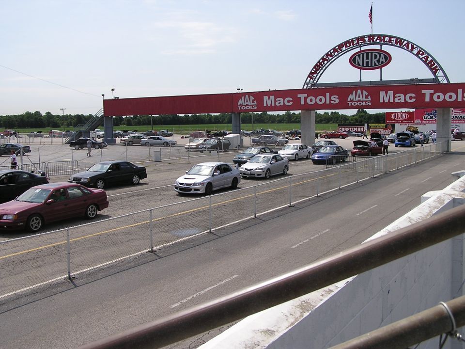 Drag strip parking lot with multiple cars, an NHRA archway, and Mac Tools banners