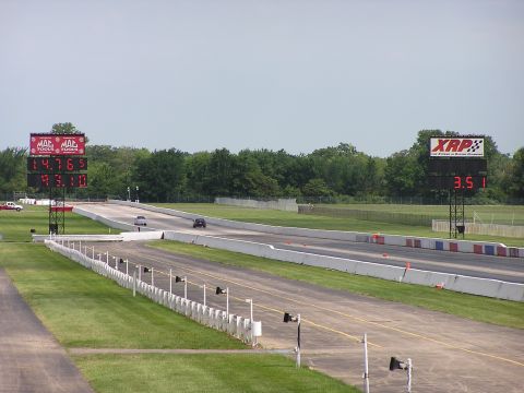 1993 Ford Taurus - A drag race is underway with two cars on the track and large digital scoreboards displaying their times.