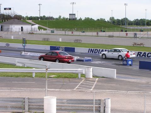 1993 Ford Taurus - Two sedans prepare for a drag race on a track with grandstands in the background.