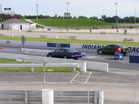 1993 Ford Taurus - Cars compete on a drag strip with grandstands and buildings in the background.