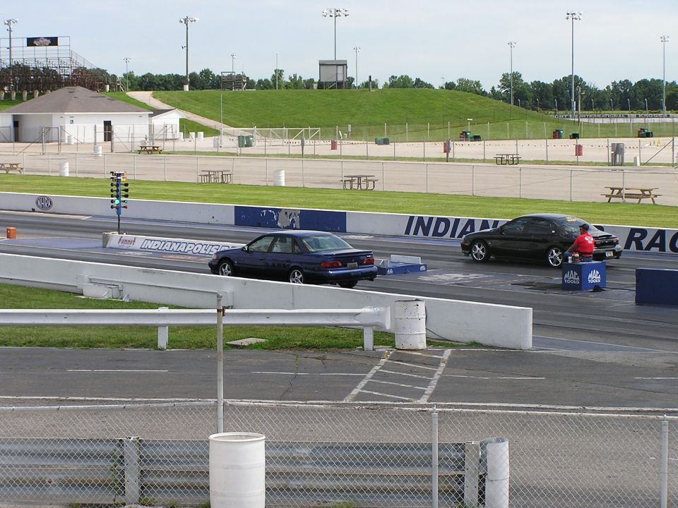 Dark blue 1993 Ford Taurus sedan in the left lane, black sedan in the right lane, on a drag strip with Indianapolis Raceway signage
