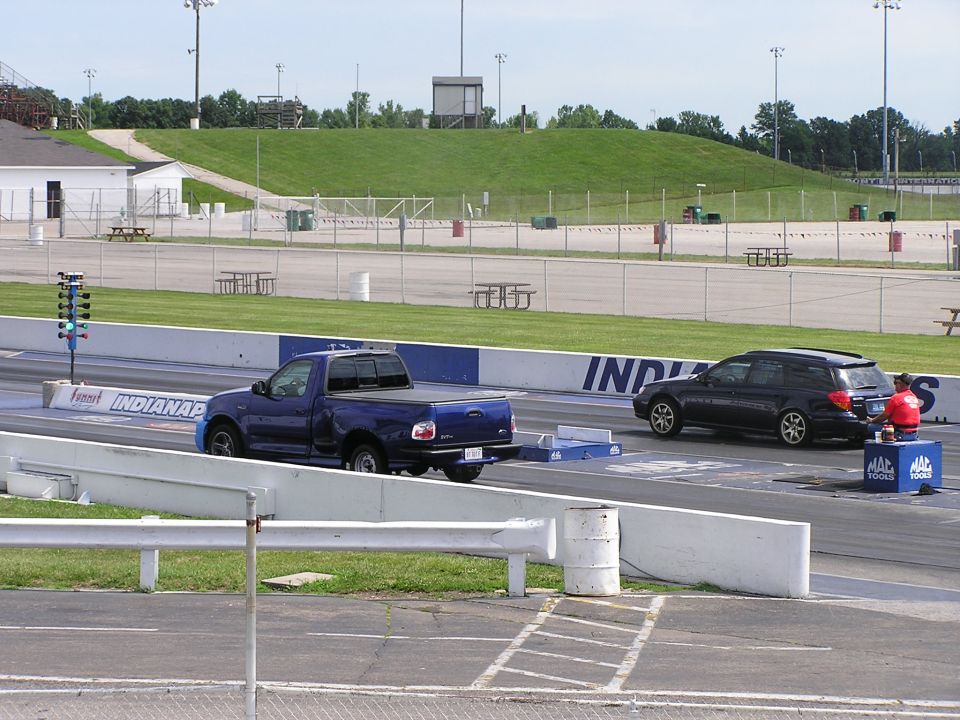 Blue Ford F-150 Lightning and black Subaru Outback at a drag strip starting line