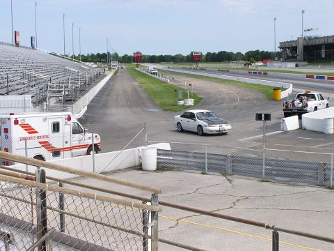 1993 Ford Taurus - Drag strip scene with an ambulance and a sedan, grandstands in the background.