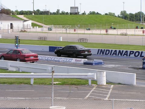 1993 Ford Taurus - Cars compete on the drag strip with grandstands and grassy hills in the background.