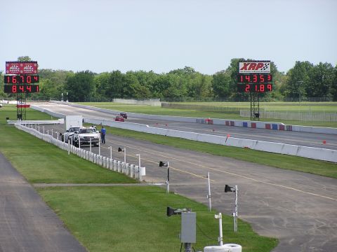 1993 Ford Taurus - Two vehicles race down a drag strip, with large digital timers displaying race times.