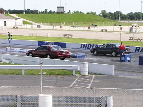 1993 Ford Taurus - Two cars prepare for a drag race on a sunny day at a track with grassy hills in the background.
