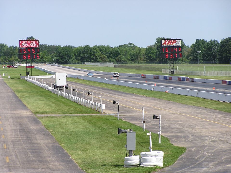 Drag strip with two cars racing, scoreboards showing times. XRP and MAC logos visible