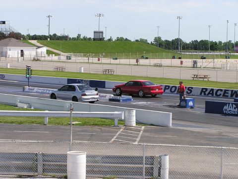 1993 Ford Taurus - A red sedan is positioned at the starting line of a drag strip, with another car visible ahead.