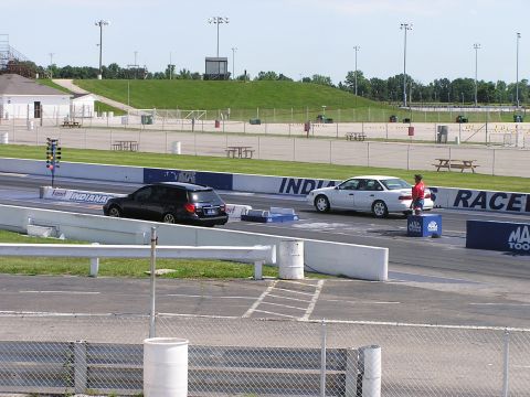 1993 Ford Taurus - A white sedan is positioned on a drag strip, with a person in a red shirt standing nearby. Another dark vehicle is visible on the adjacent…
