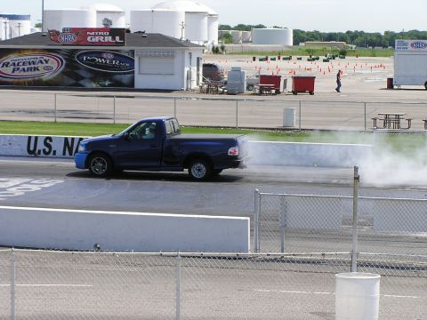1993 Ford Taurus - A blue pickup truck speeds down the drag strip, emitting a cloud of smoke from its exhaust.