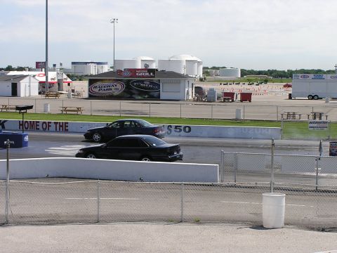 1993 Ford Taurus - Two sedans compete on a drag strip, with industrial tanks visible beyond the track.