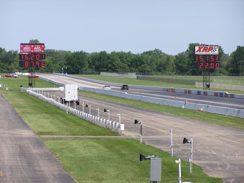 1993 Ford Taurus - Two cars compete on a drag strip, with large digital scoreboards displaying their race times.