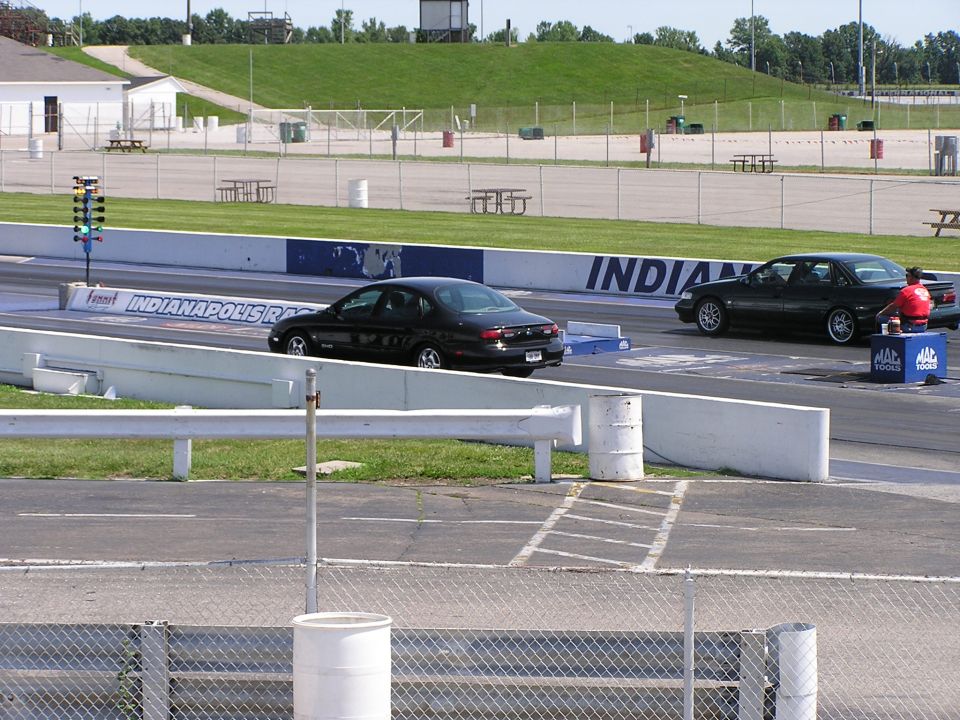 Two black sedans, one appearing to be a 1993 Ford Taurus, on a drag strip with starting lights