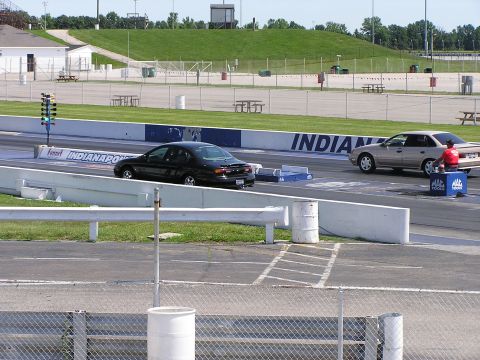 1993 Ford Taurus - Two sedans are lined up on a drag strip, with a person in red sitting on a toolbox next to the tan car.