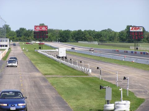 1993 Ford Taurus - A blue 1993 Ford Taurus is seen on a drag strip, with other vehicles and scoreboards visible in the background.