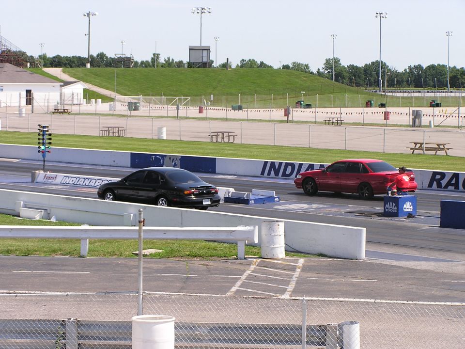Red 1993 Ford Taurus and black sedan on drag strip, side view