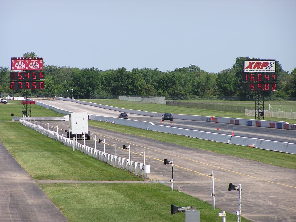 Cars race down a drag strip with large digital timers showing times