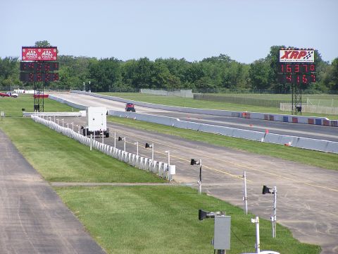 1993 Ford Taurus - A red car races down a drag strip, with large digital scoreboards displaying times.