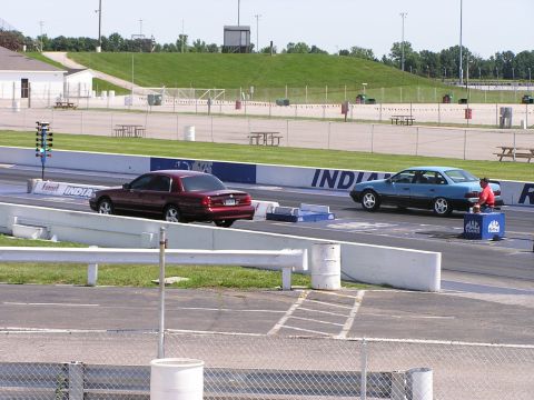 1993 Ford Taurus - Two cars are lined up on a drag strip, ready for a race, with a person attending to one of the vehicles.