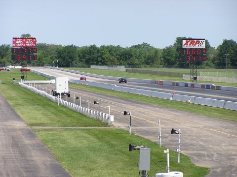 1993 Ford Taurus - Drag strip scene with two cars on the track and large digital scoreboards displaying race times.