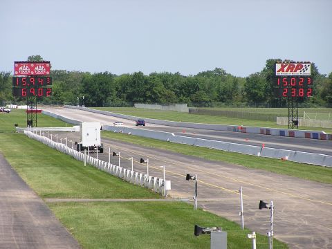 1993 Ford Taurus - Two cars compete on a drag strip under a clear sky, with digital timers displaying their performance.