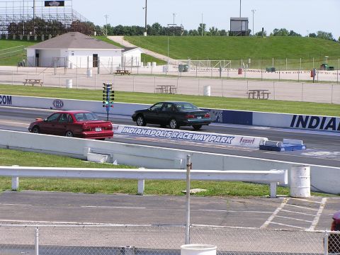 1993 Ford Taurus - Two sedans compete on the drag strip at Indianapolis Raceway Park, with a Christmas tree starting system visible.