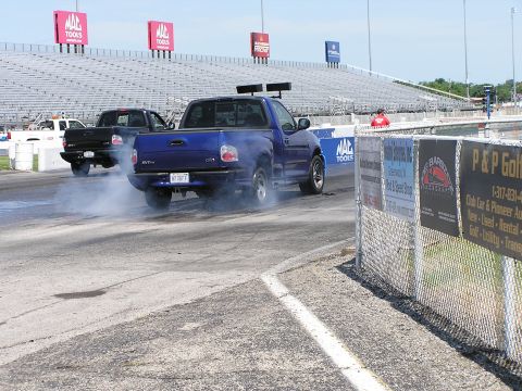 1993 Ford Taurus - Two pickup trucks race down a drag strip, kicking up smoke during a burnout.