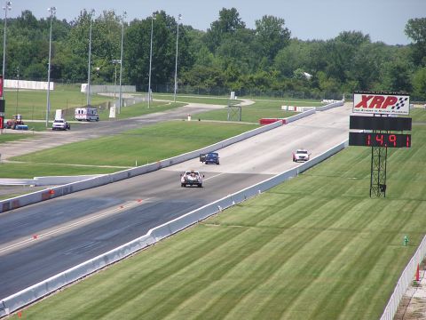 1993 Ford Taurus - Cars race down a drag strip with a large electronic scoreboard displaying the time.