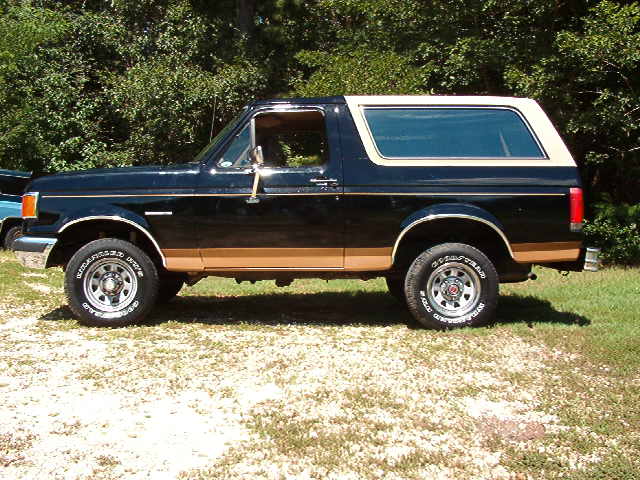 Side view of a black Ford Bronco with tan trim. It has a removable hardtop