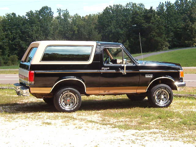 Black and tan Ford Bronco parked on grass, side view
