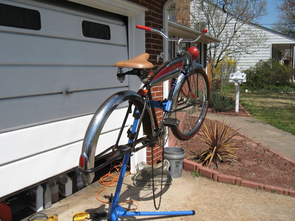vintage bicycle with chrome fenders and tan seat on a blue repair stand, in front of a garage door