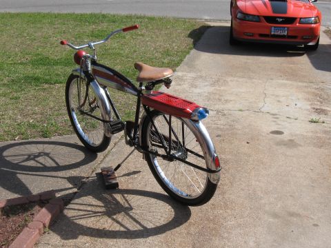 1994 Ford Bronco - A vintage bicycle with red handlebars and seat sits on a concrete driveway next to an orange car.