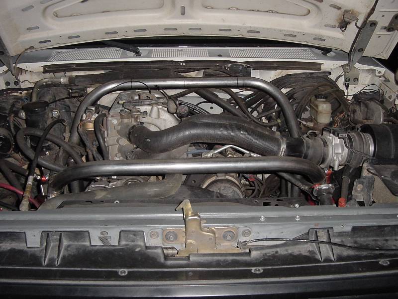 Engine bay with custom bare-metal tubular brace over engine, black hoses and wiring